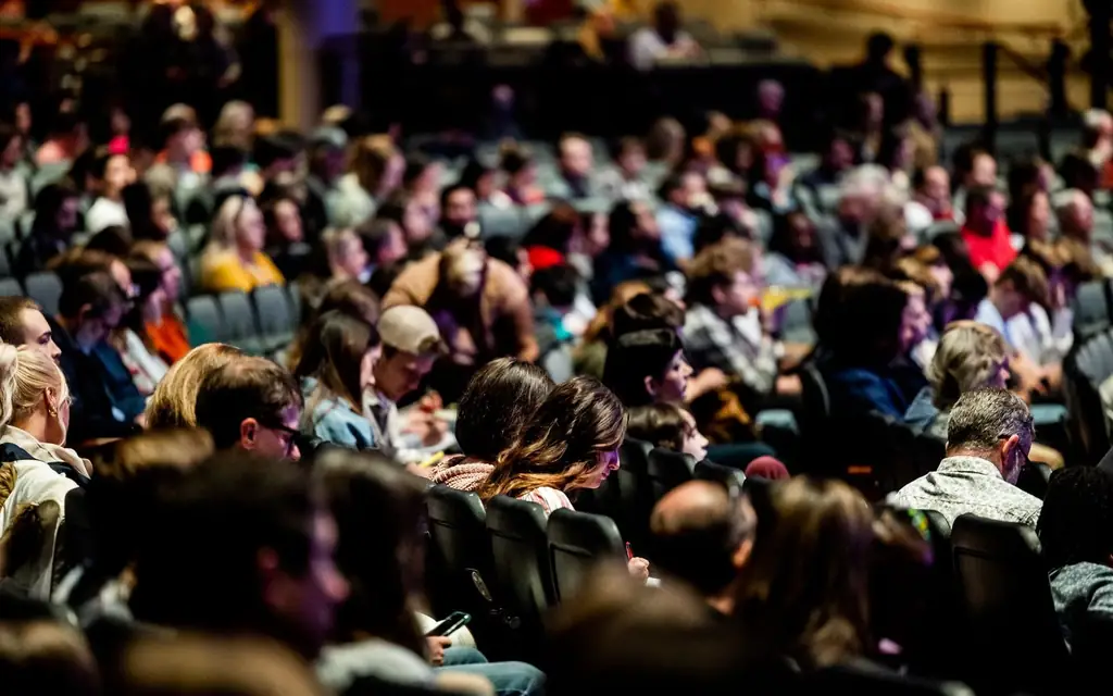A diverse crowd seated in an auditorium, engaged in an indoor event