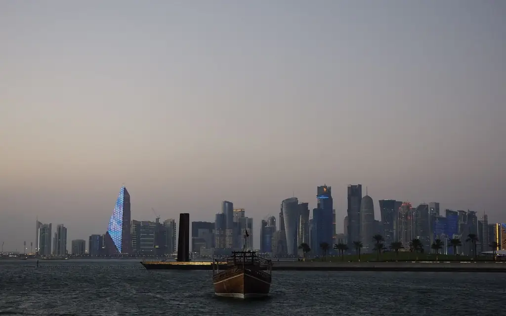 Scenic view of Doha city skyline with traditional dhow boat at dusk along the waterfront